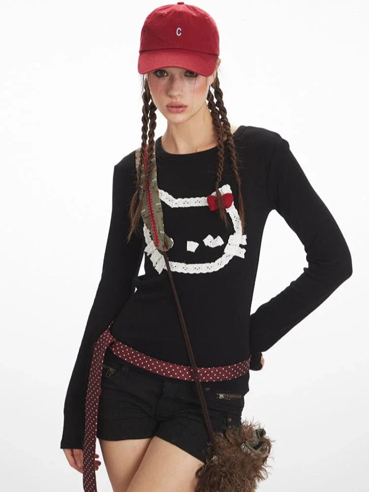 Woman posing in a black long-sleeved shirt with a cat graphic print, black shorts, and camouflage boots.