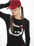 Detailed view of the graphic print on a black long-sleeved shirt, featuring a cat face with applique details and a red bow.