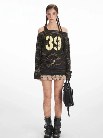 Woman wearing a camouflage print off-shoulder long sleeve top with a "39 1949" graphic print, paired with a denim skirt and boots.