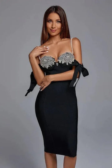 Woman wearing a black bodycon midi dress with a sweetheart neckline, pearl shoulder straps, and decorative bows on the sleeves.